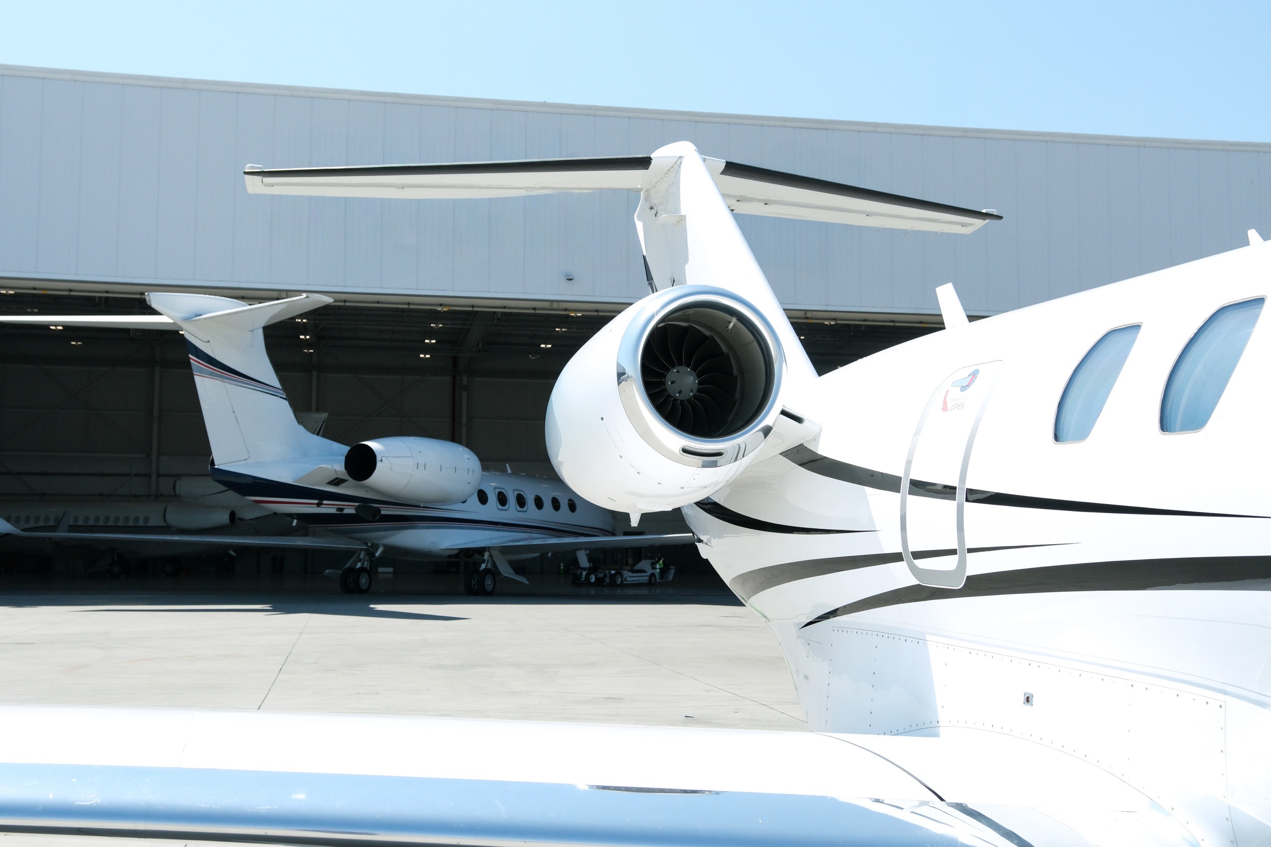 Close up of the Cessna Citation X private jet on the tarmac with silver trim and swept tail near a hangar.