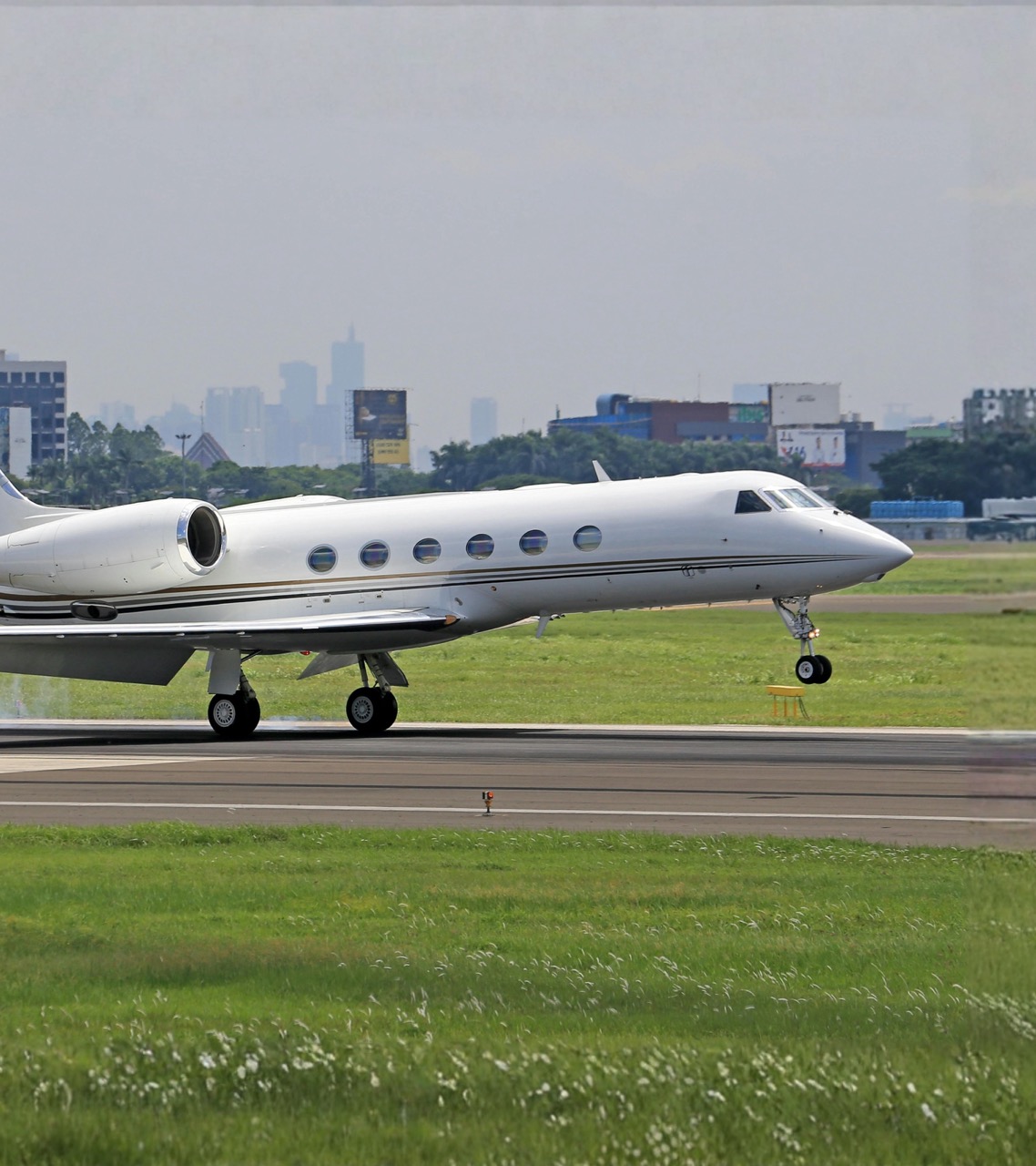 Gulfstream G550 private jet landing on runway with landing gear down during touchdown at international airport.