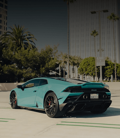 Teal Lamborghini Huracán parked in a palm tree lined Miami street.